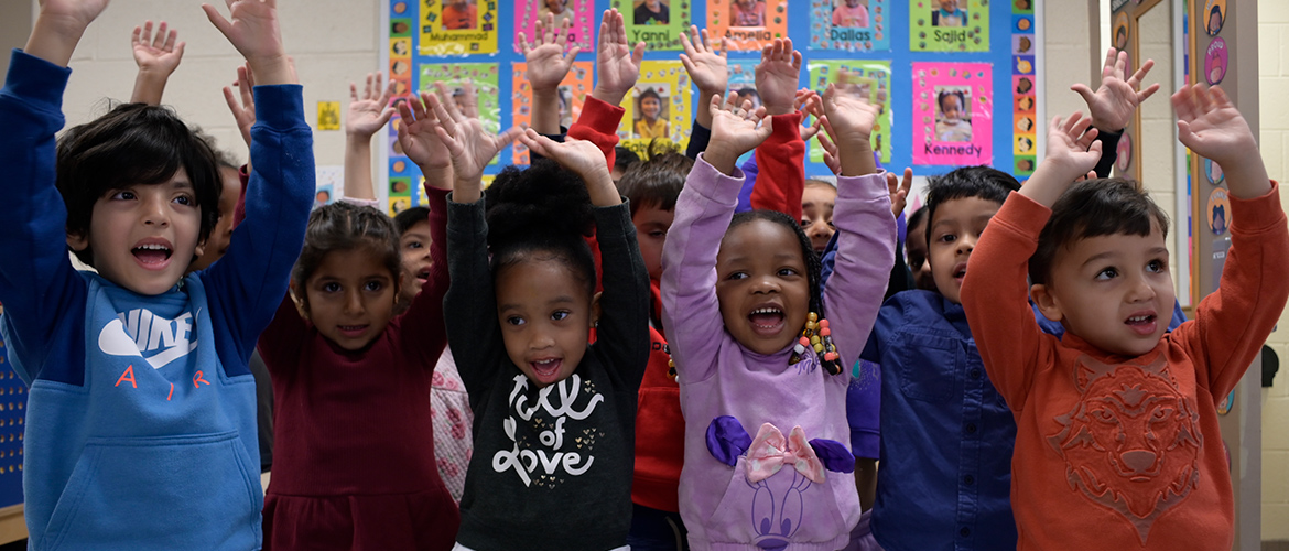 Children raise their hands in their elementary classroom