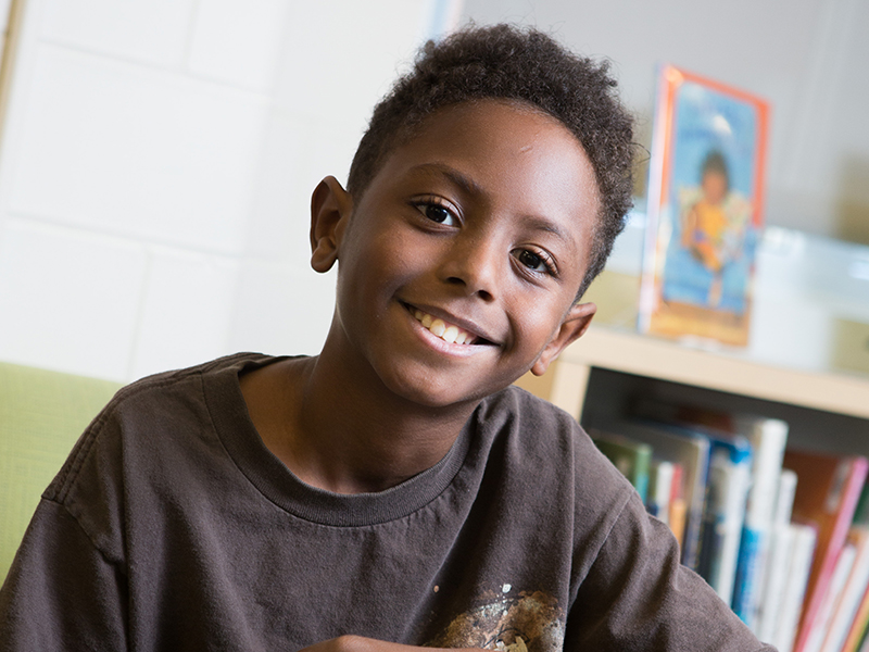 A young black boy smiles at the camera in his classroom
