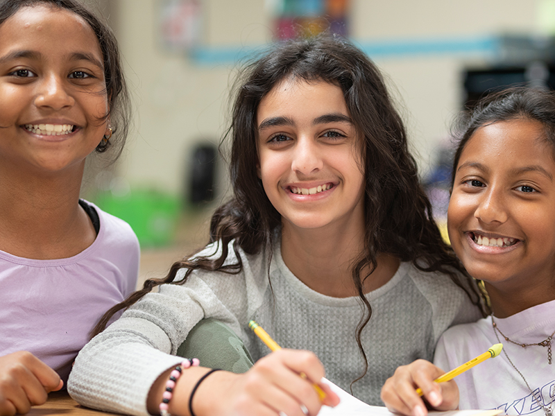 Three girls smile in their middle school classroom